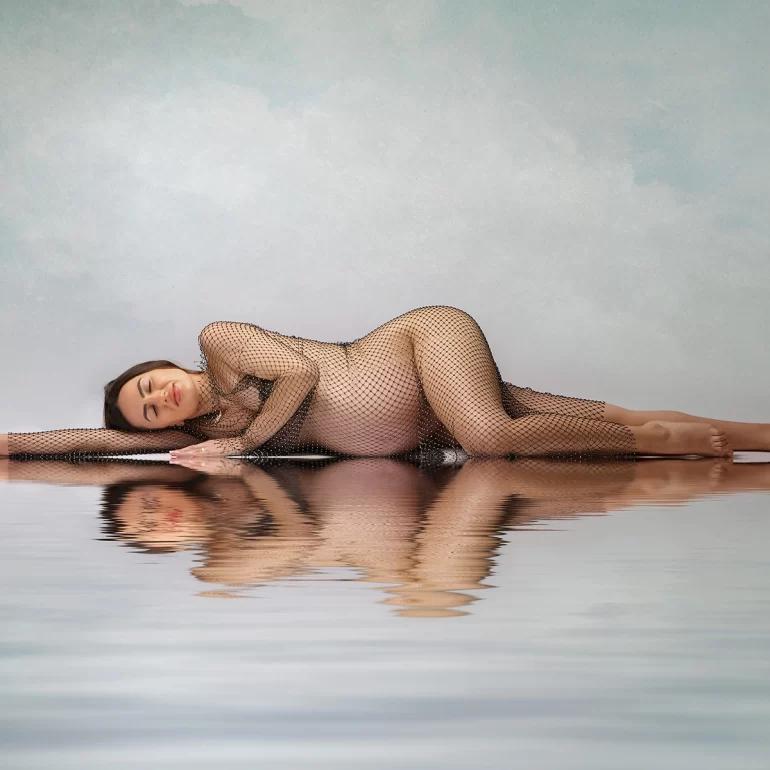 Maternity Photoshoot in North West London 24 Reclining on reflective surface; shimmering mesh gown, pastel background.