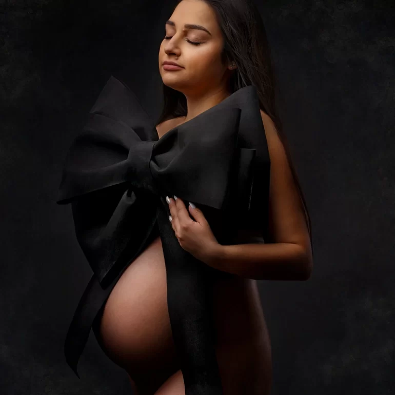 Maternity Photoshoot in North West London 57 Oversized black bow; closed eyes and calm expression; textured dark background.