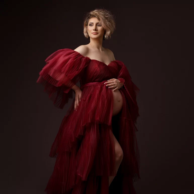 Maternity Photoshoot in North West London 58 Layered burgundy gown; gentle hand on belly; dramatic studio light.