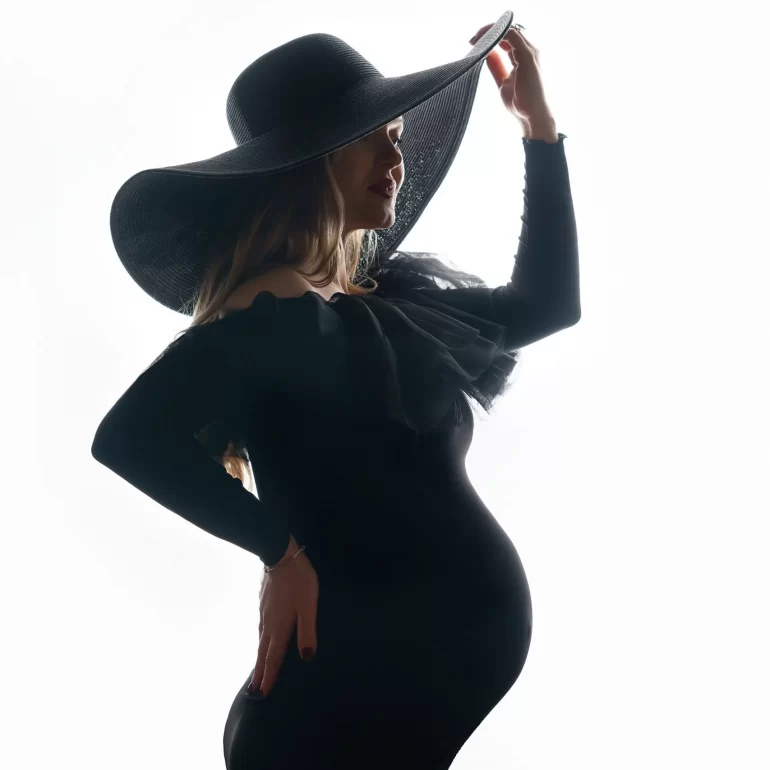 Maternity Photoshoot in North West London 59 Off‑shoulder black dress and wide‑brim hat; high‑contrast silhouette.