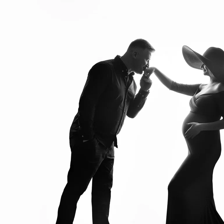 Maternity Photoshoot in North West London 62 B&W couple; he kisses her hand; wide‑brim hat; refined elegance.