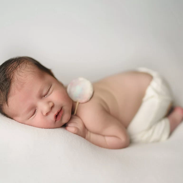 Newborn Photoshoot in North West London 13 Baby on white blanket with pastel felt lollipop; clean, minimal setup.
