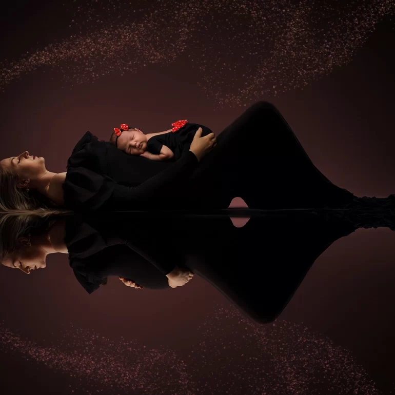 Newborn Photoshoot in North West London 14 Mother in black gown with baby; golden bokeh arc and mirrored reflection.