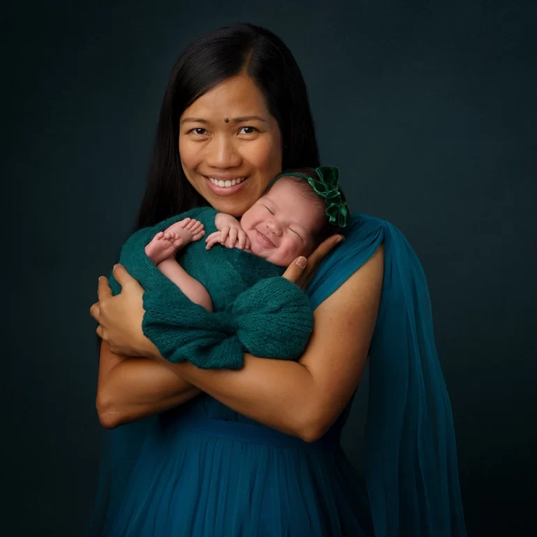 Newborn Photoshoot in North West London 17 Mother in teal gown holding baby in matching swaddle; warm, joyful portrait.
