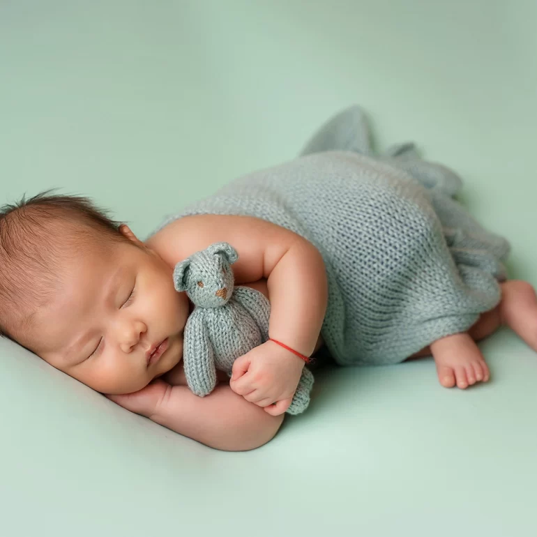 Newborn Photoshoot in North West London 20 Baby on mint backdrop holding knit teddy; soft, pastel palette.