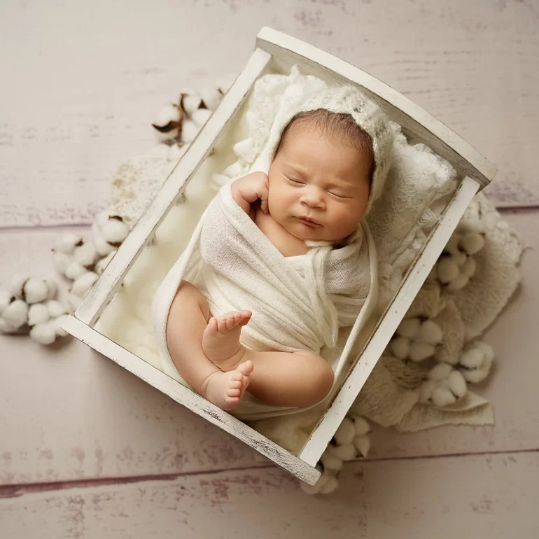 Newborn Photoshoot in North West London 30 Baby in white wrap sleeping in wooden crate with cotton accents.