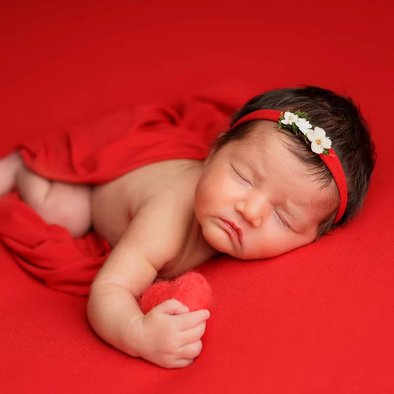 Newborn Photoshoot in North West London 41 Baby on vivid red with floral headband and felt heart; matching wrap.