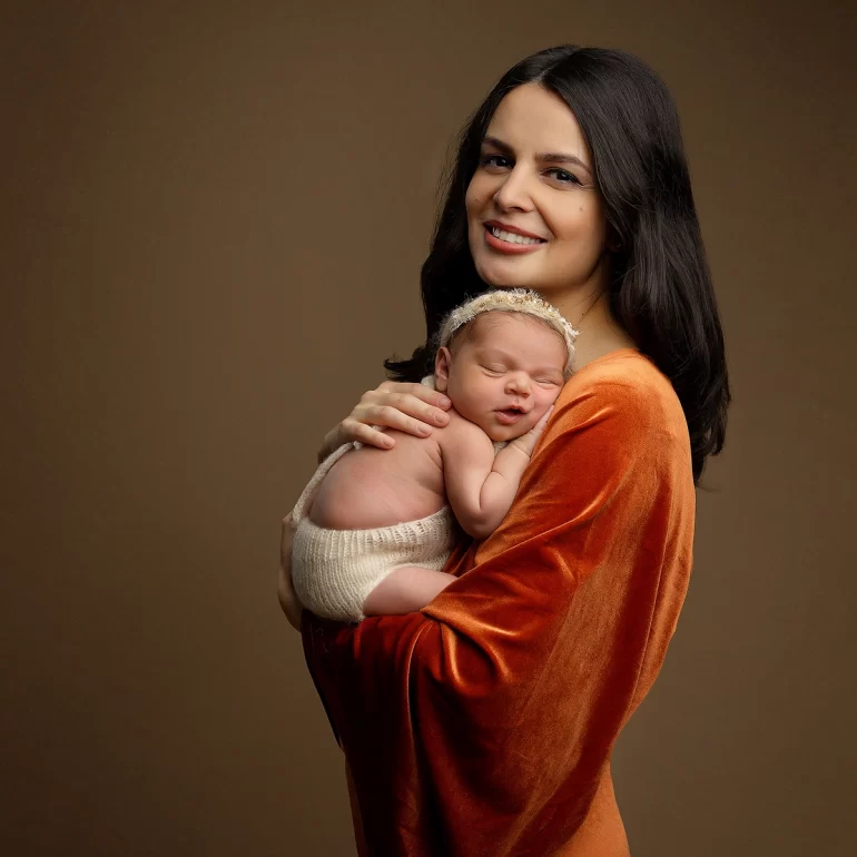 Newborn Photoshoot in North West London 49 Mother in orange velvet with baby in cream knit; earthy backdrop, elegant.