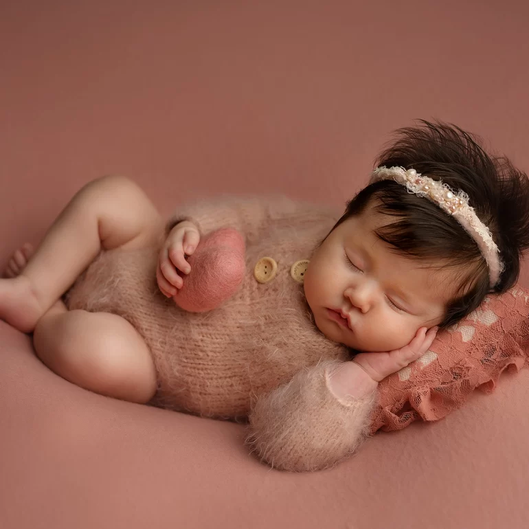 Newborn Photoshoot in North West London 50 Baby girl on lace pillow in pink knit with pearl headband; holding felt heart.