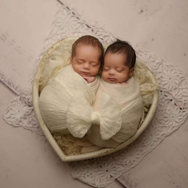 Newborn Photoshoot in North West London 8 Sleeping twins in creamy wraps inside heart bowl; lace details, warm light.