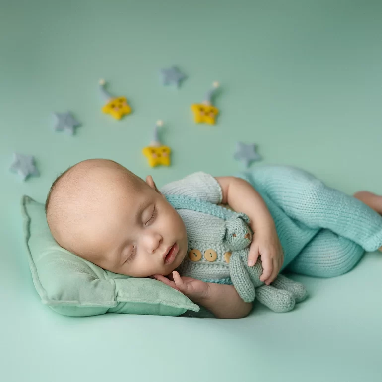 Newborn Photoshoot in North West London 54 Baby on mint pillow in knit romper, holding teddy; stars and moon décor.