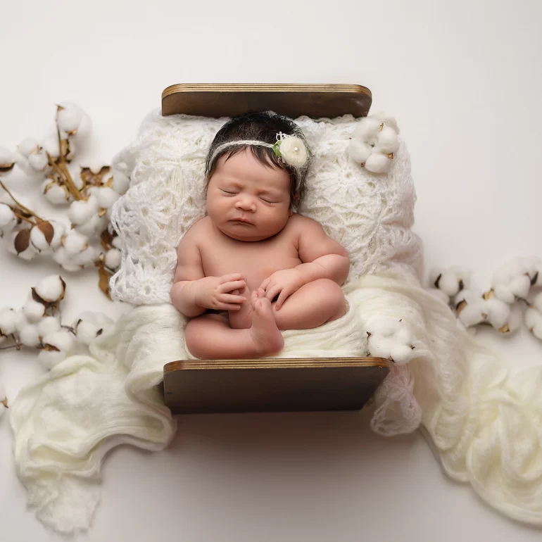 Newborn Photoshoot in North West London 56 Baby in rustic wooden bed with cotton accents and floral headband; pure, serene.