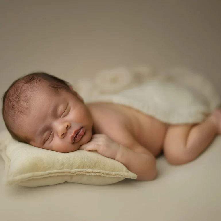 Newborn Photoshoot in North West London 64 Baby asleep on cream pillow with ivory blanket; minimalist beige backdrop.