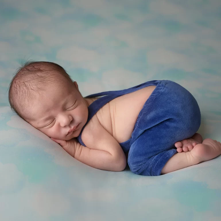 Newborn Photoshoot in North West London 67 Baby in soft blue overalls on cloud backdrop; light, airy and dreamy.