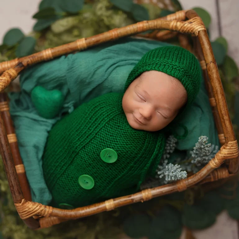 Newborn Photoshoot in North West London 69 Baby in vibrant green knit with hat in wicker basket; greenery surrounds.