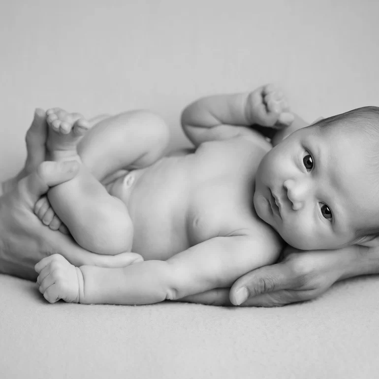 Newborn Photoshoot in North West London 70 B&W baby cradled in parents’ hands; minimalist, tender connection.