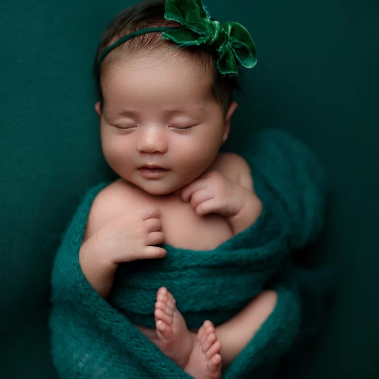 Newborn Photoshoot in North West London 72 Baby in emerald knit with velvet bow headband; deep green backdrop, soothing.