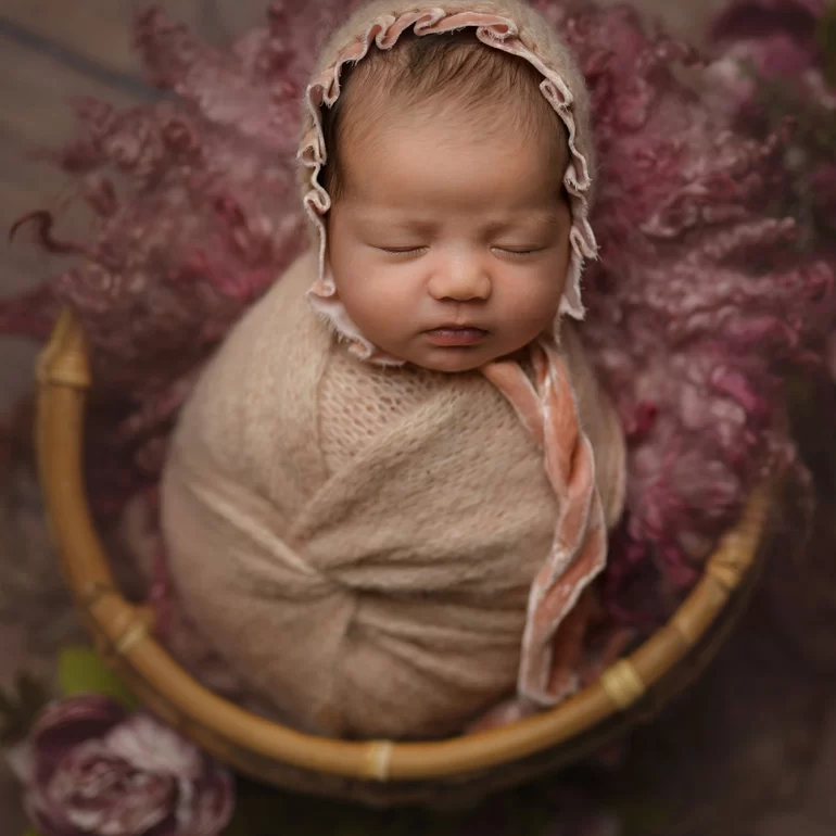 Newborn Photoshoot in North West London 76 Baby in beige wrap with ruffled bonnet in basket; dusty pink florals.