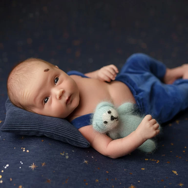 Newborn Photoshoot in North West London 82 Awake baby in blue overalls with teddy on starry backdrop; heart‑shaped birthmark.