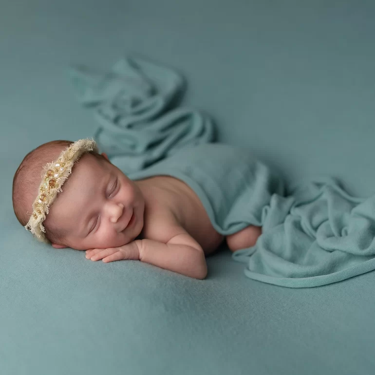 Newborn Photoshoot in North West London 11 Baby on teal blanket with pearl headband; soft swaddle and gentle smile.