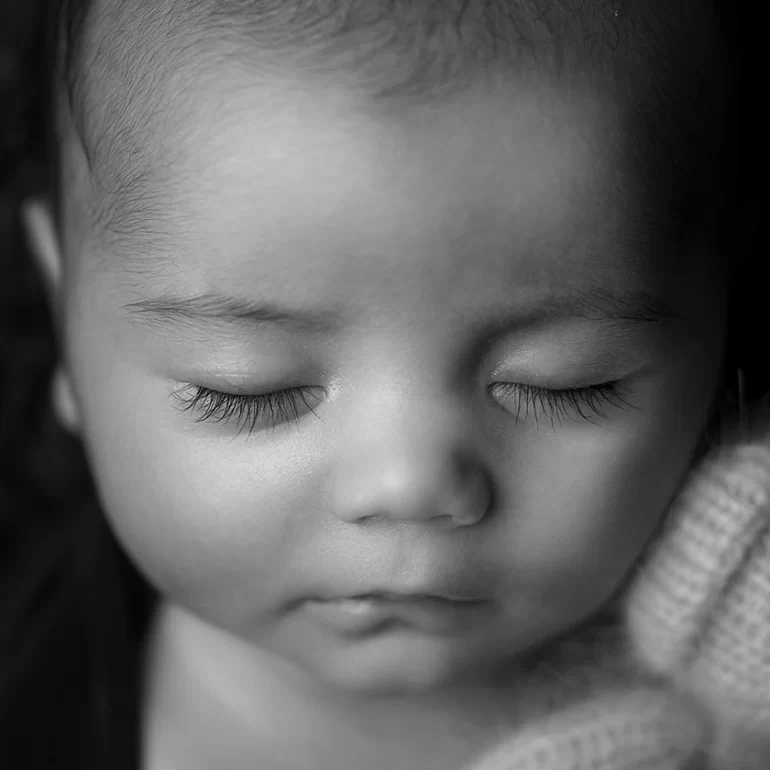 Newborn Photoshoot in North West London 86 B&W close‑up of sleeping baby holding tiny knit teddy; delicate lashes.