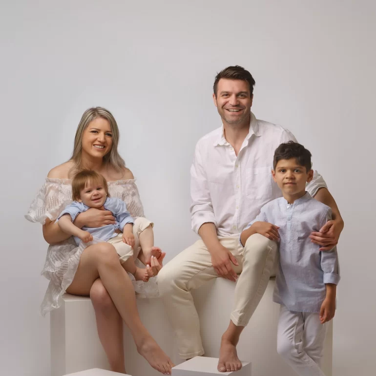 Family & Portrait Photoshoot in North West London 4 Family of four in light outfits on white studio set; mother holding baby.