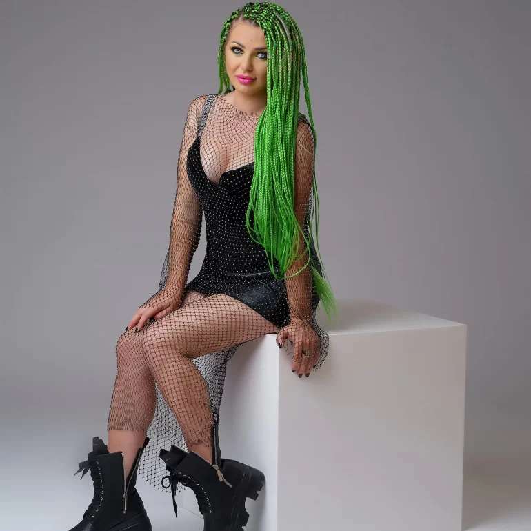 Family & Portrait Photoshoot in North West London 14 Woman with green braids in black outfit and boots seated on white cube; grey backdrop.