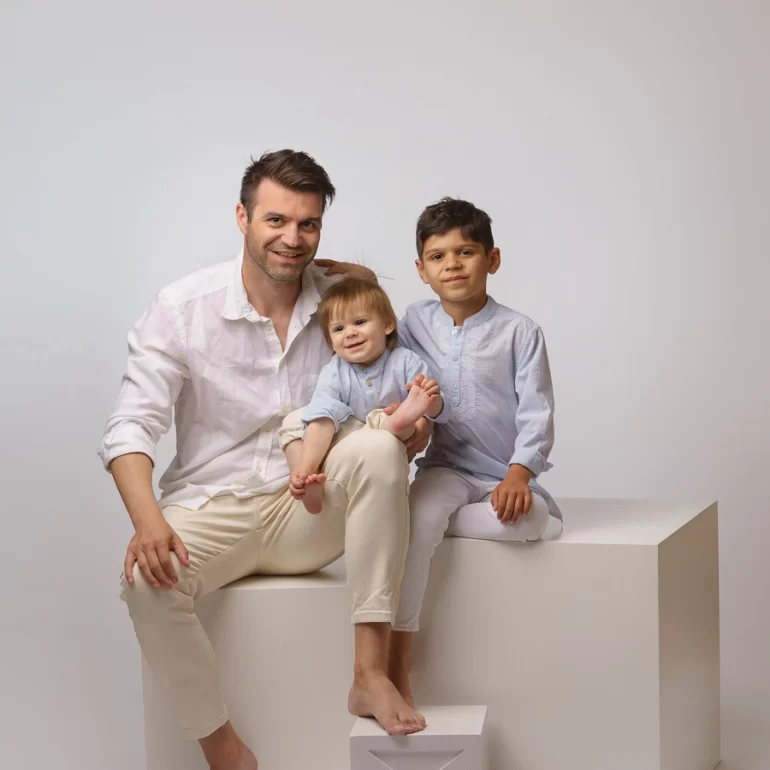 Family & Portrait Photoshoot in North West London 12 Father and two boys in light outfits seated on white cubes; bright studio, warm smiles.