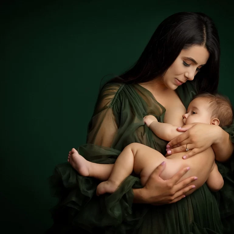 Family & Portrait Photoshoot in North West London 31 Mother breastfeeding baby in elegant green gown against rich green backdrop.