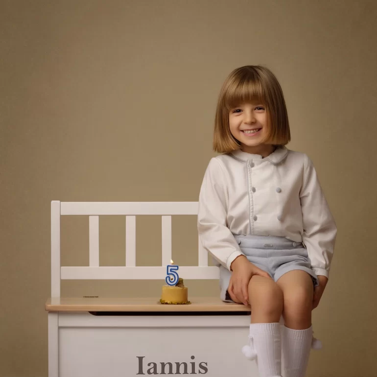 Family & Portrait Photoshoot in North West London 32 Young boy in white and light blue sitting on white bench with name plaque; cheerful pose.