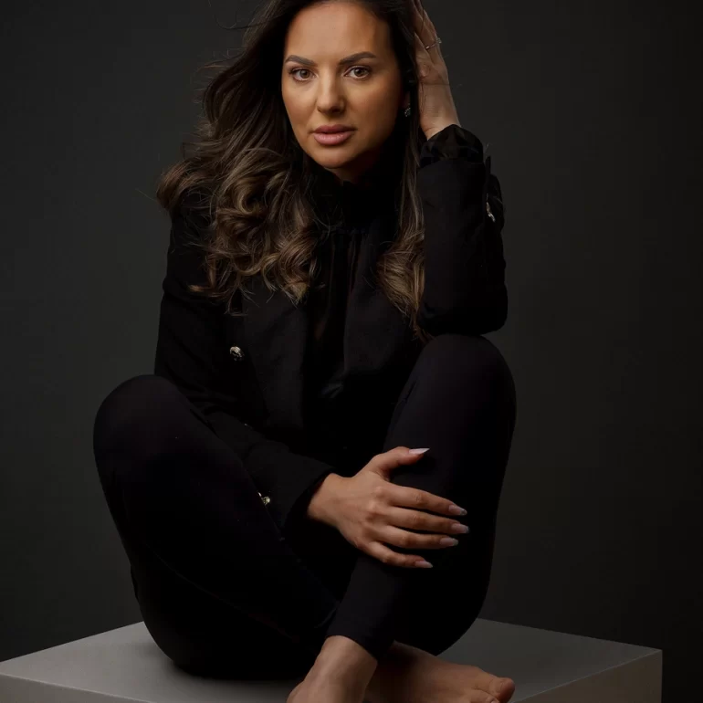 Family & Portrait Photoshoot in North West London 36 Woman in elegant black seated barefoot on white cube; confident gaze, dark backdrop.
