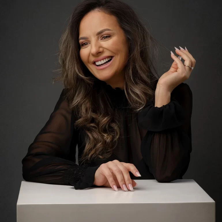 Family & Portrait Photoshoot in North West London 6 Woman with wavy hair in sheer black blouse leaning on white cube; dark studio.