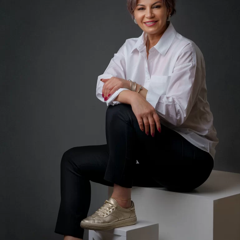 Family & Portrait Photoshoot in North West London 11 Short‑haired woman in white shirt and gold sneakers seated on white cubes; dark backdrop.