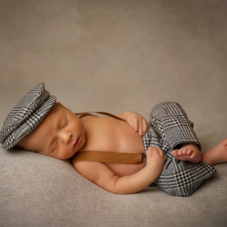Newborn Photoshoot in North West London 3 Baby in plaid suspenders and cap on beige set; softly lit, timeless.