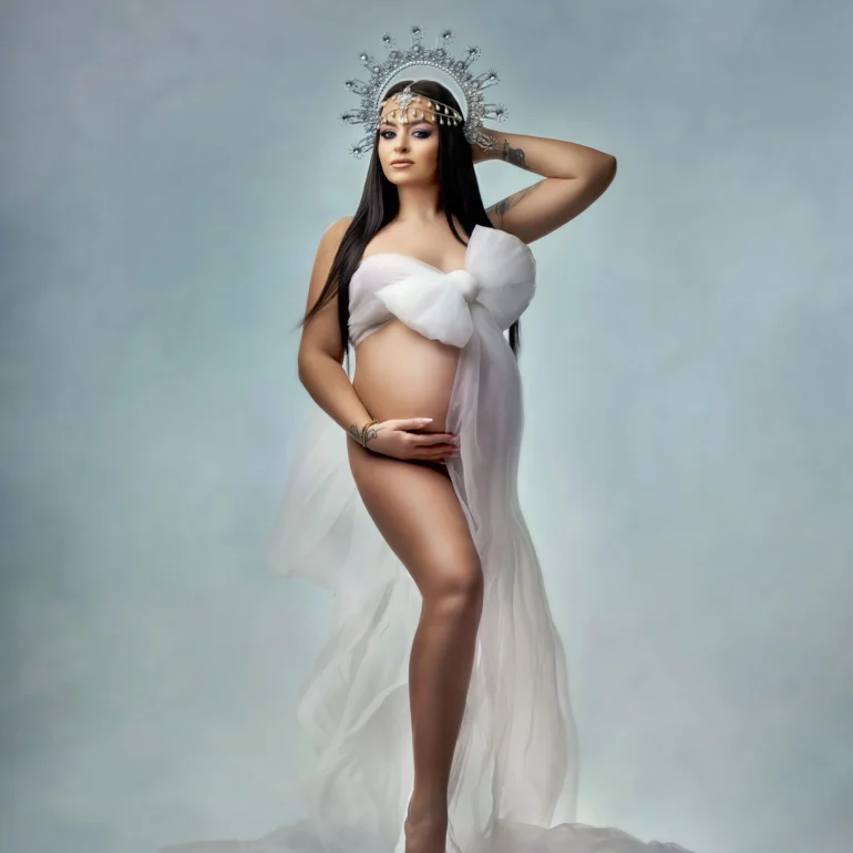 Maternity Photoshoot in North West London 52 White bow‑styled fabric and crystal crown; barefoot on soft blue.