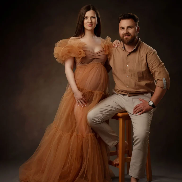 Maternity Photoshoot in North West London 80 Light‑brown ruffled gown; seated partner; earthy, serene tones.