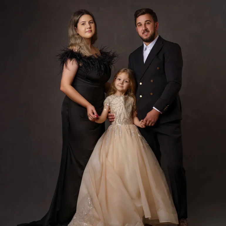 Family & Portrait Photoshoot in North West London 3 Couple with young daughter in beige gown posing together against a dark studio background.