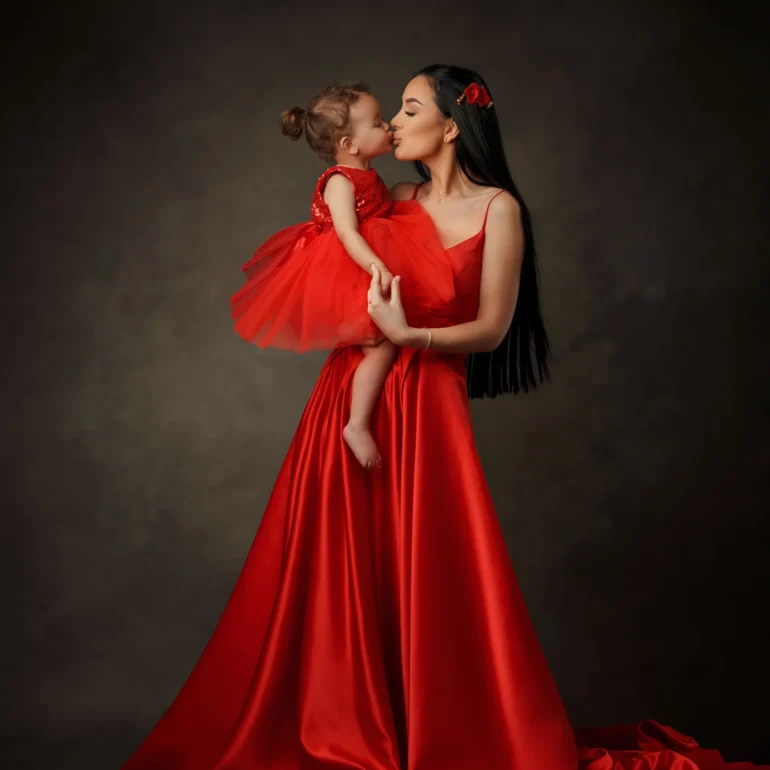 Family & Portrait Photoshoot in North West London 60 Mother in flowing red gown kissing daughter in matching dress; dark studio background.