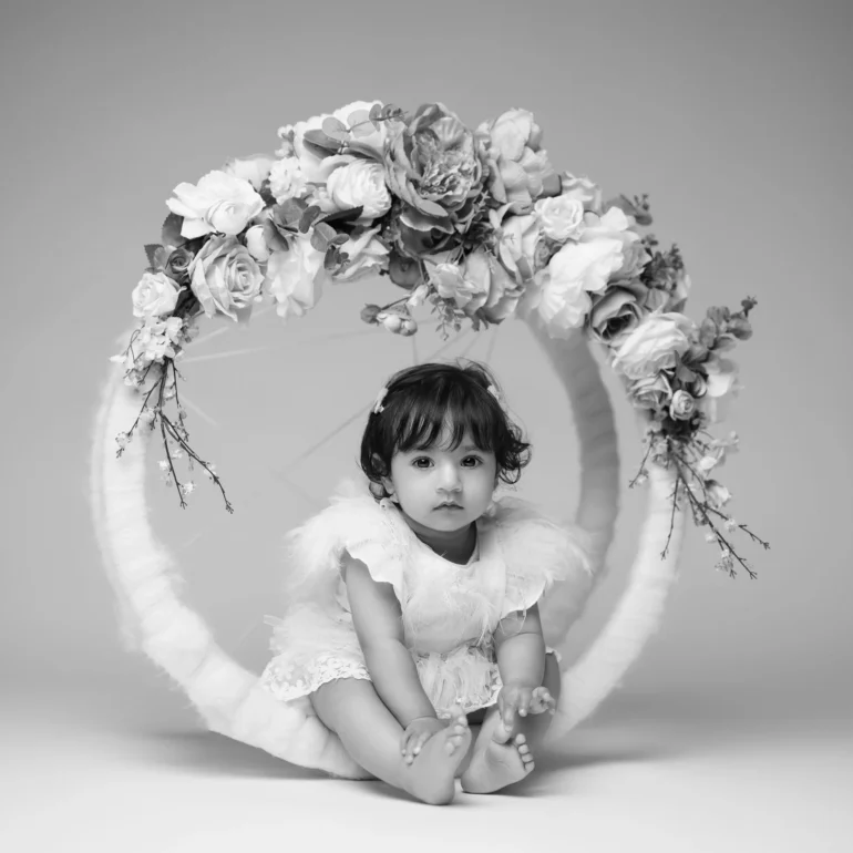 Family & Portrait Photoshoot in North West London 55 Baby girl in feather‑accented outfit seated inside floral ring; minimalist black‑and‑white.