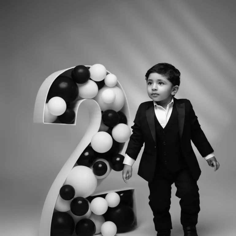 Family & Portrait Photoshoot in North West London 46 Young boy in black suit beside number 2 prop filled with black and white balloons.